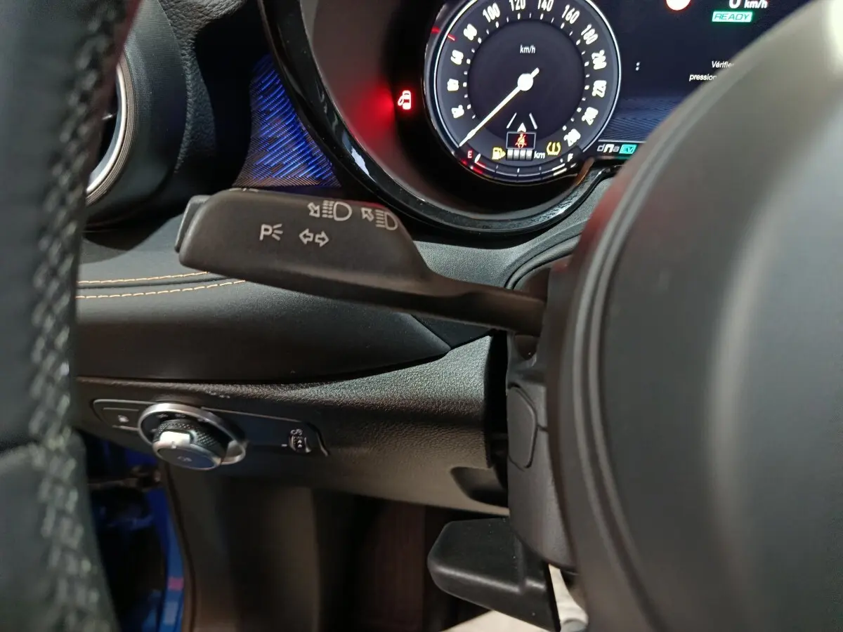 Gros plan intérieur sur le volant et le combiné d'instruments numérique de l'Alfa Romeo Tonale bleu, avec commandes et éclairage ambiant.