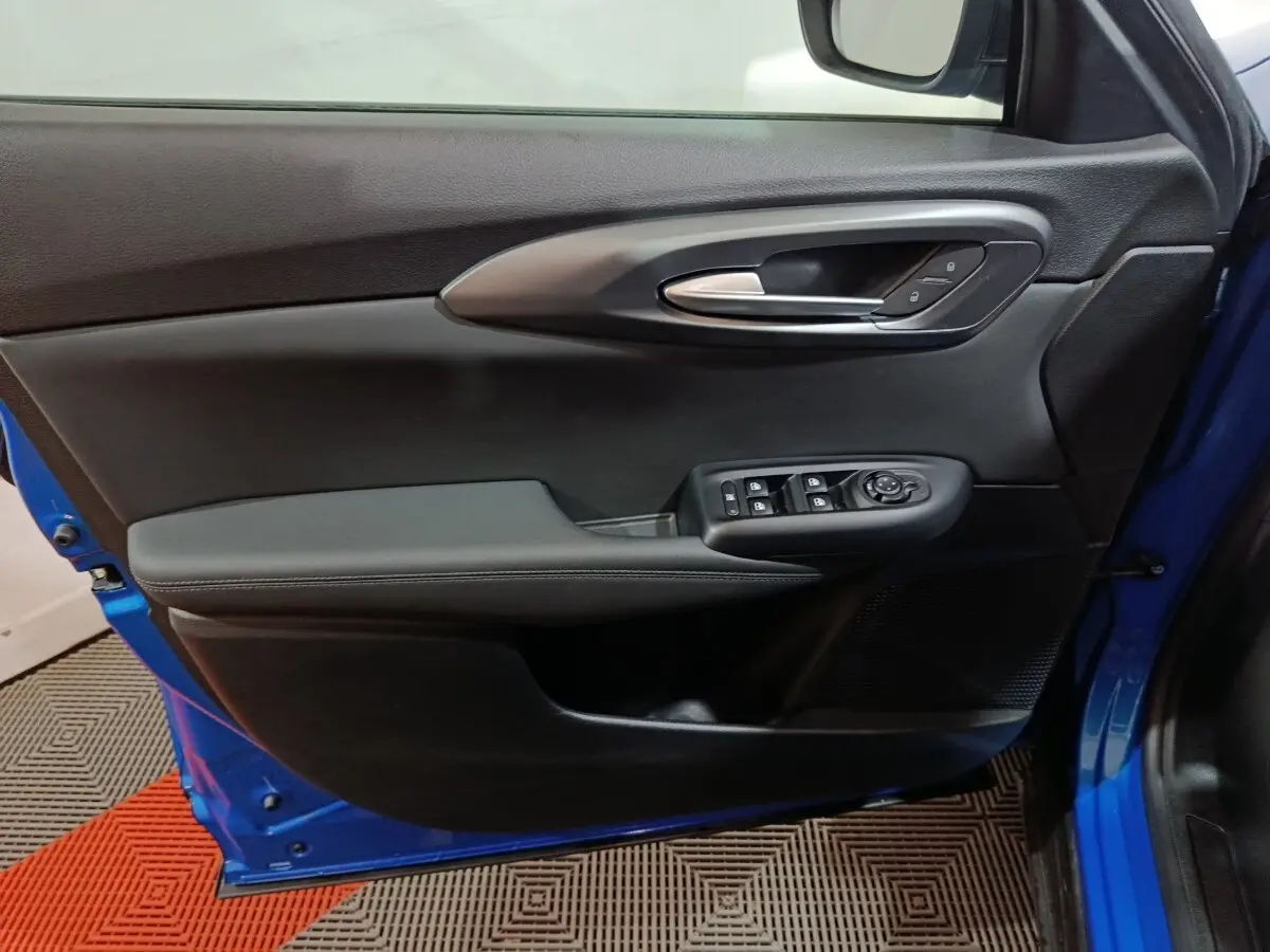 Vue intérieure côté gauche de la porte avant bleu de l'Alfa Romeo Tonale avec commandes de vitres et poignée argentée.