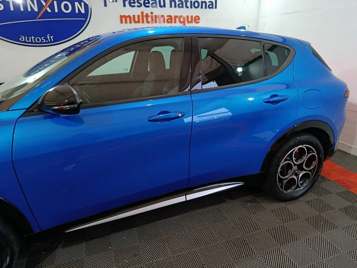 Vue latérale côté gauche d'un Alfa Romeo Tonale bleu 2023 avec jantes distinctives à cinq cercles et poignées de porte ton caisse.