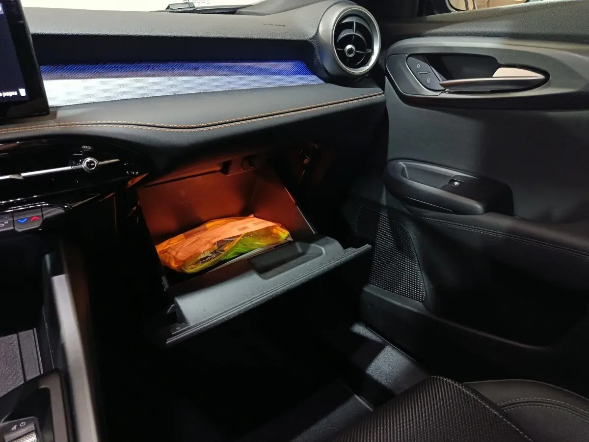 Intérieur de l'Alfa Romeo Tonale 2023, vue côté passager, boîte à gants ouverte avec éclairage orange.