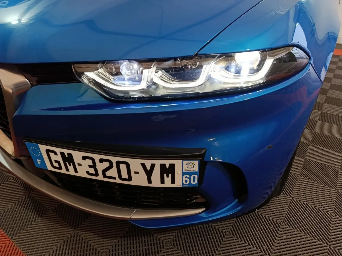 Gros plan sur l'avant droit bleu vif de l'Alfa Romeo Tonale 2023 avec phares LED allumés et plaque d'immatriculation française.