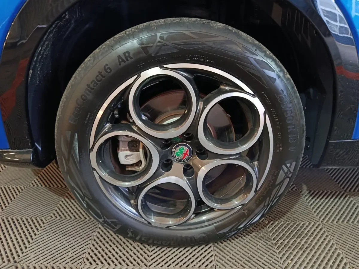 Gros plan sur la roue avant droite de l'Alfa Romeo Tonale bleu, avec jante distinctive à cinq cercles et logo central.