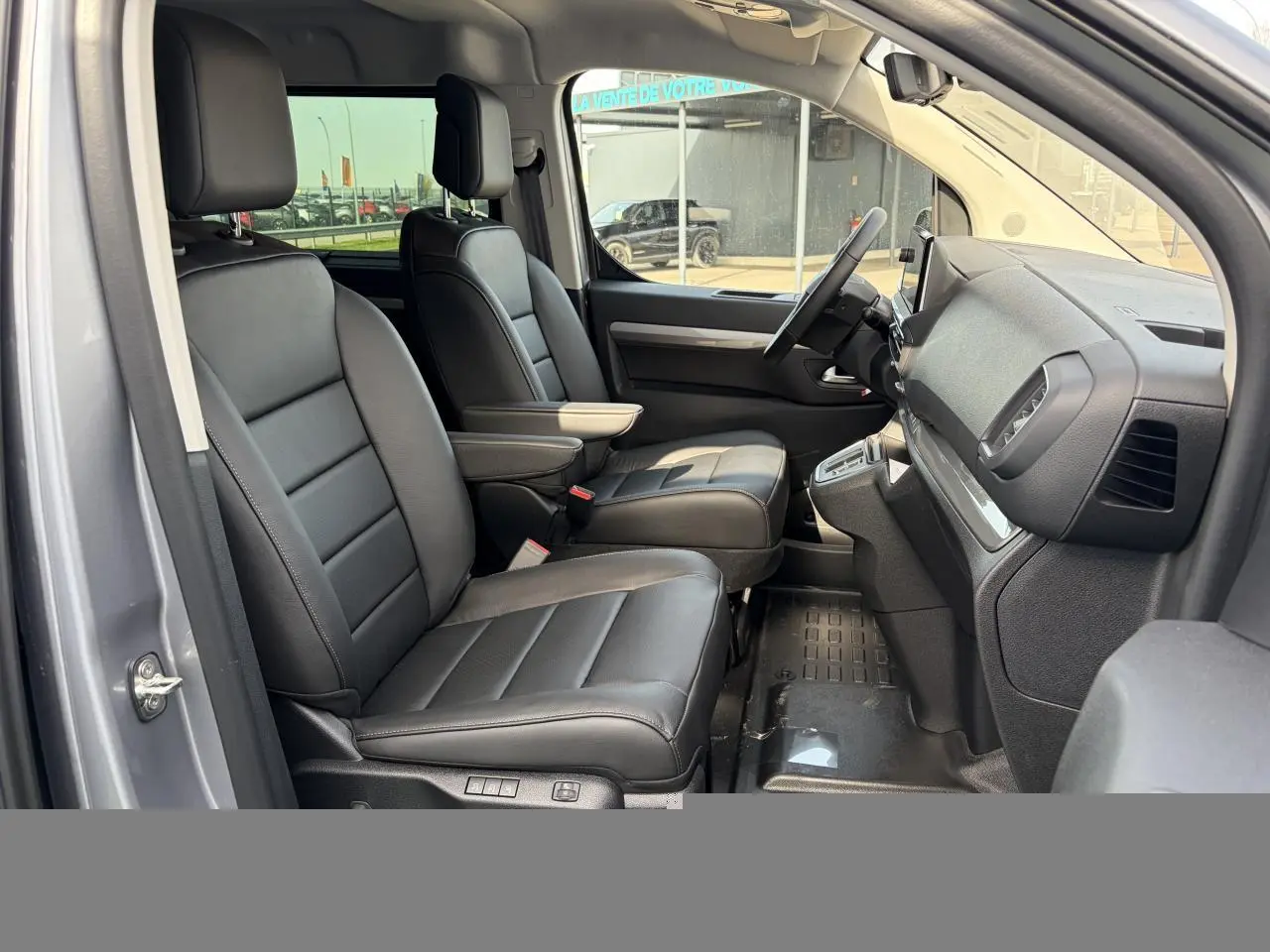 Vue intérieure côté gauche du Citroën Jumpy gris acier, montrant les sièges avant en cuir noir avec accoudoirs.