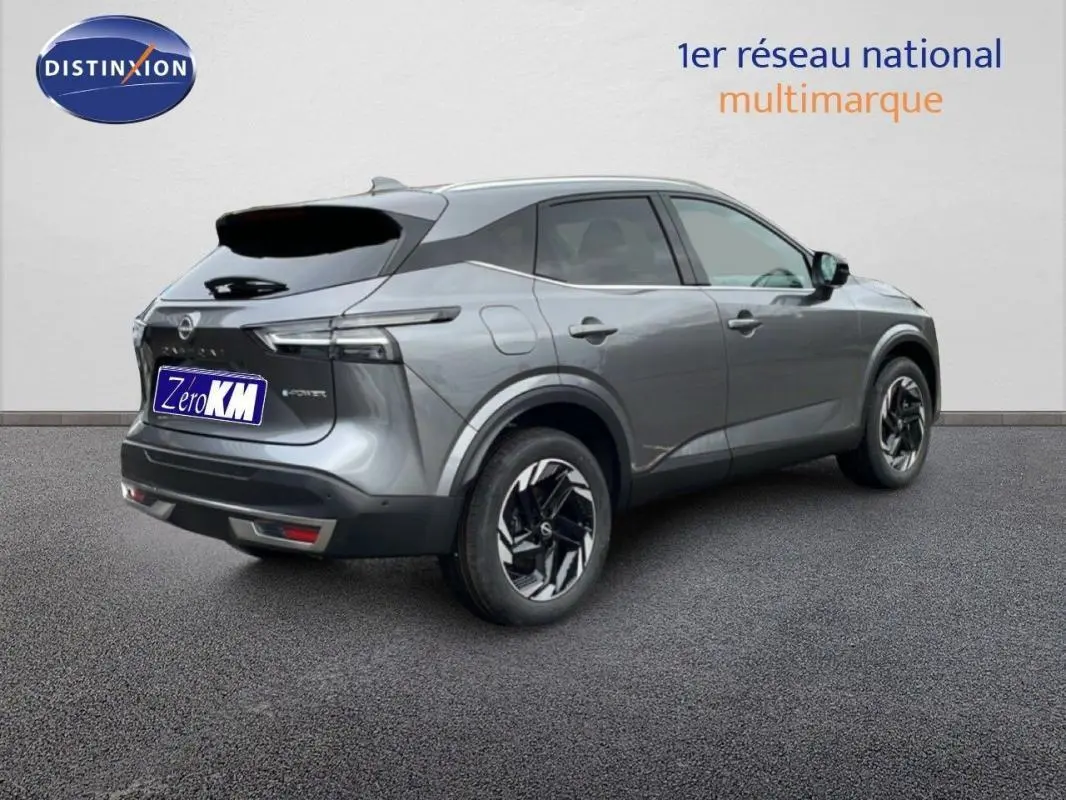 Vue 3/4 arrière droite d'un Nissan Qashqai gris 2025 avec jantes aluminium et barres de toit visibles.