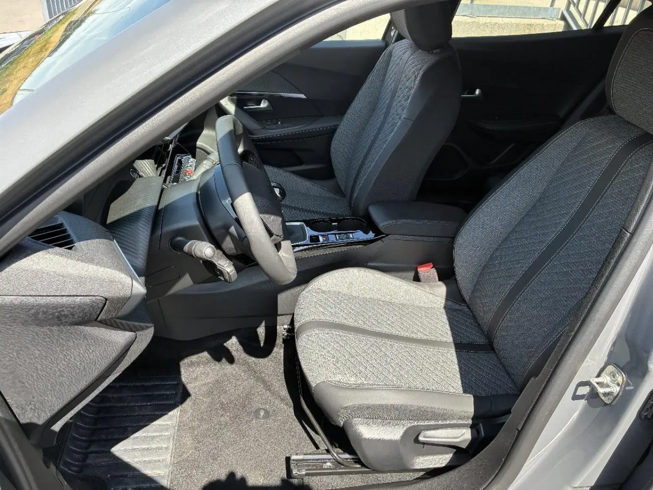 Vue intérieure côté conducteur du Peugeot 2008 2024, sièges tissu gris avec surpiqûres et volant compact.