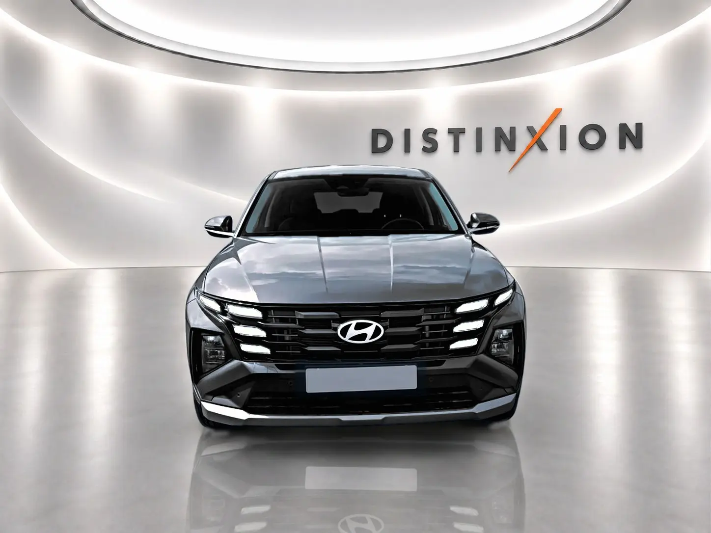 Vue frontale d'un Hyundai Tucson 2026 gris ecotronique avec calandre noire et éclairage LED distinctif, sur fond blanc lumineux.