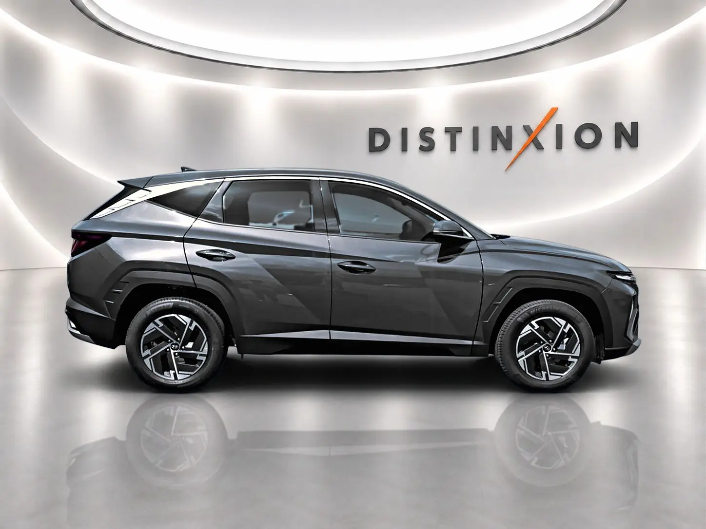 Vue de profil côté gauche du Hyundai Tucson 2026 gris ecotronique avec jantes alliage 17 pouces dans un showroom lumineux.