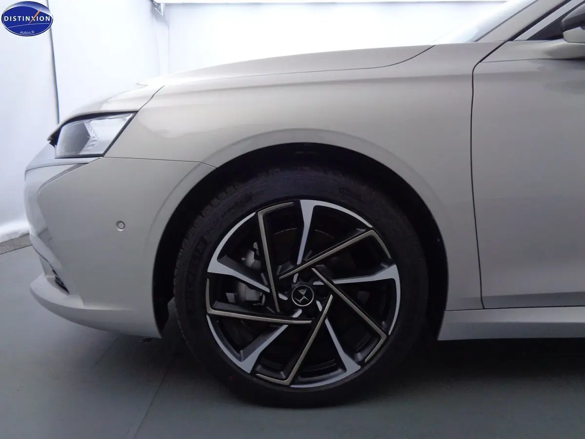 Gros plan sur la roue avant gauche de la DS9 hybride en Crystal Pearl nacré, soulignant la jante noire et argentée au design moderne.