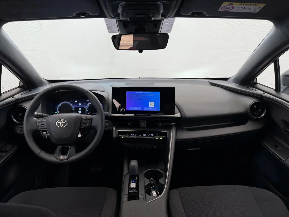 Intérieur noir du Toyota C-HR 1.8 Hybride 2024 vu de face, tableau de bord avec écran tactile central allumé.