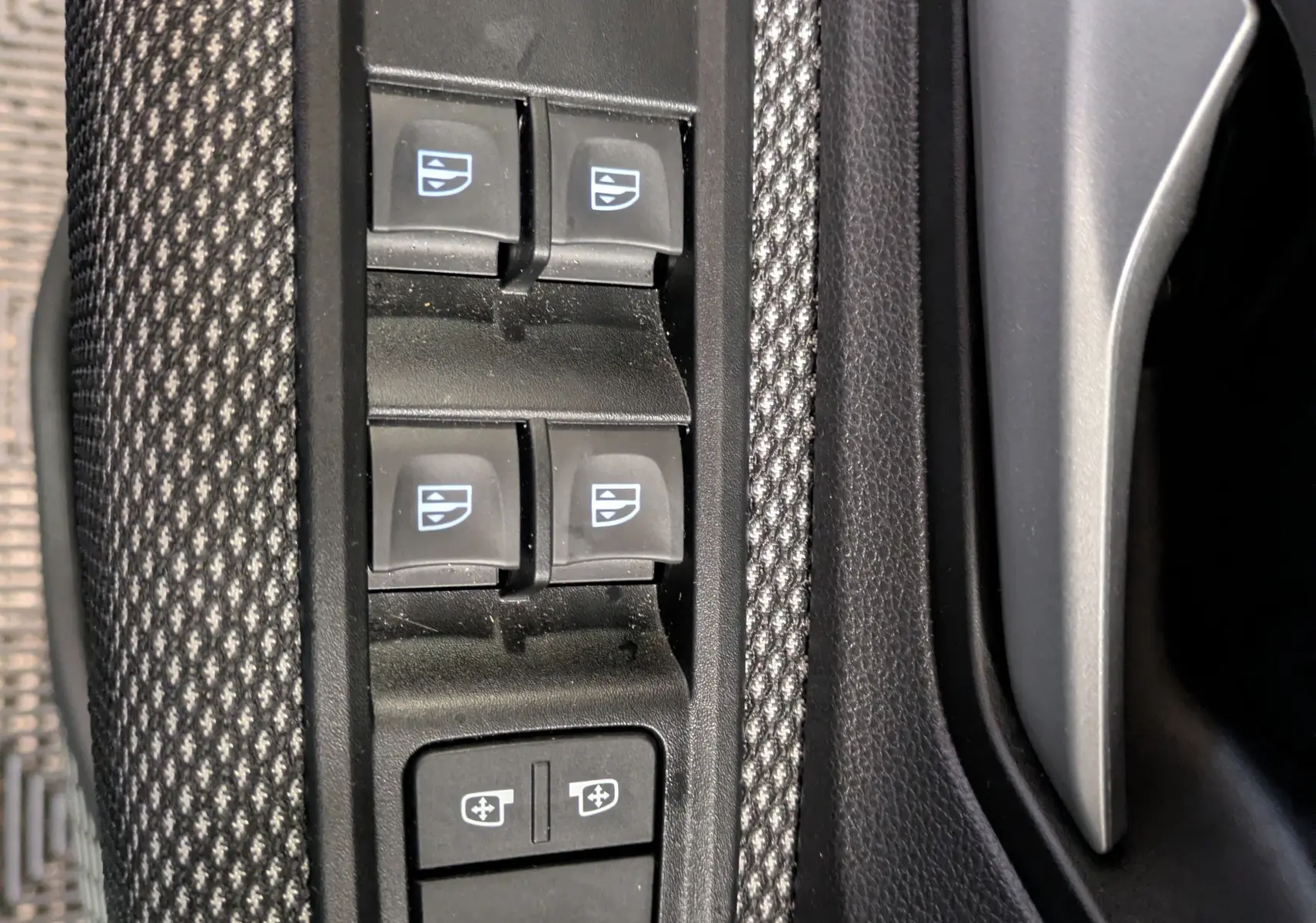 Gros plan sur les commandes des vitres électriques et réglages des rétroviseurs côté conducteur du Dacia Jogger gris schiste.