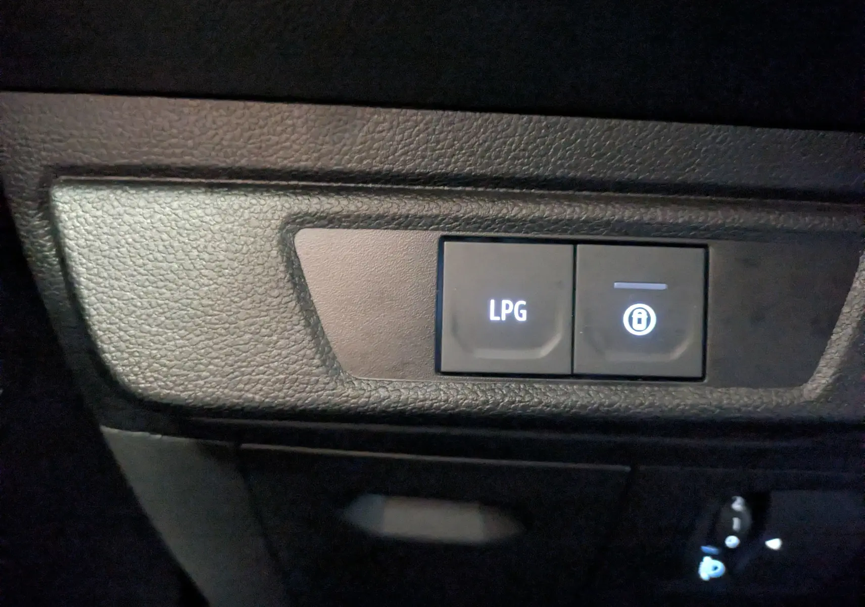 Gros plan sur les boutons de commande LPG et verrouillage intérieur du tableau de bord du Dacia Jogger gris schiste.