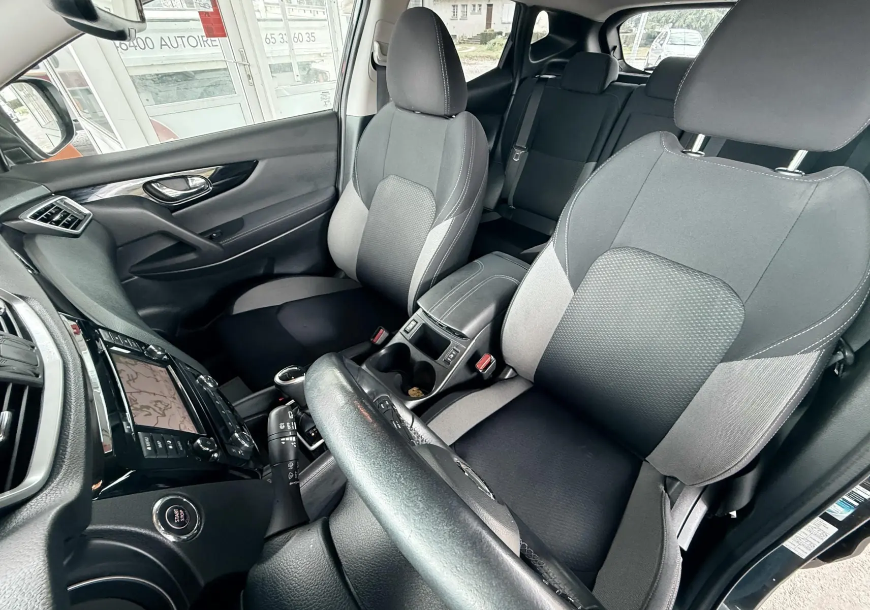 Vue intérieure du Nissan Qashqai 2020 côté conducteur, sièges tissu noir et gris, tableau de bord avec écran tactile.