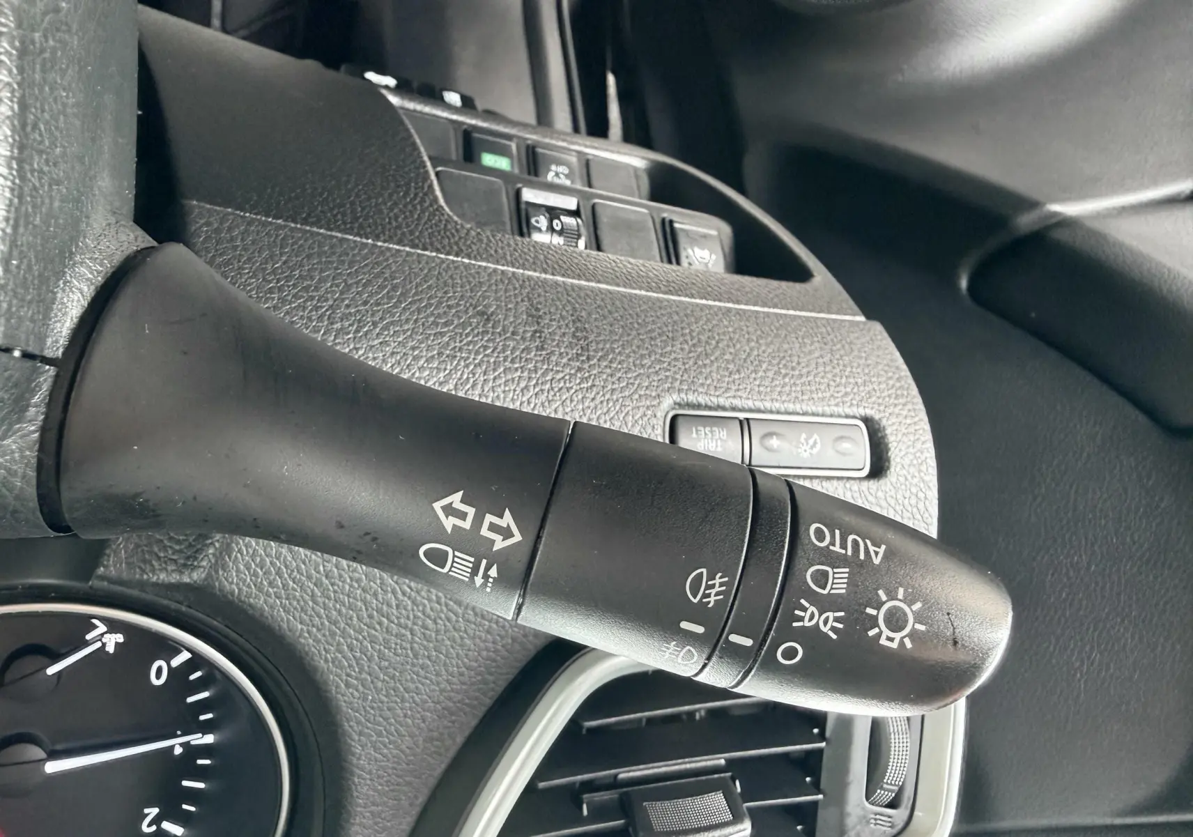 Gros plan sur la manette de commandes d’éclairage noire à gauche du volant dans l’habitacle d’un Nissan Qashqai noir.