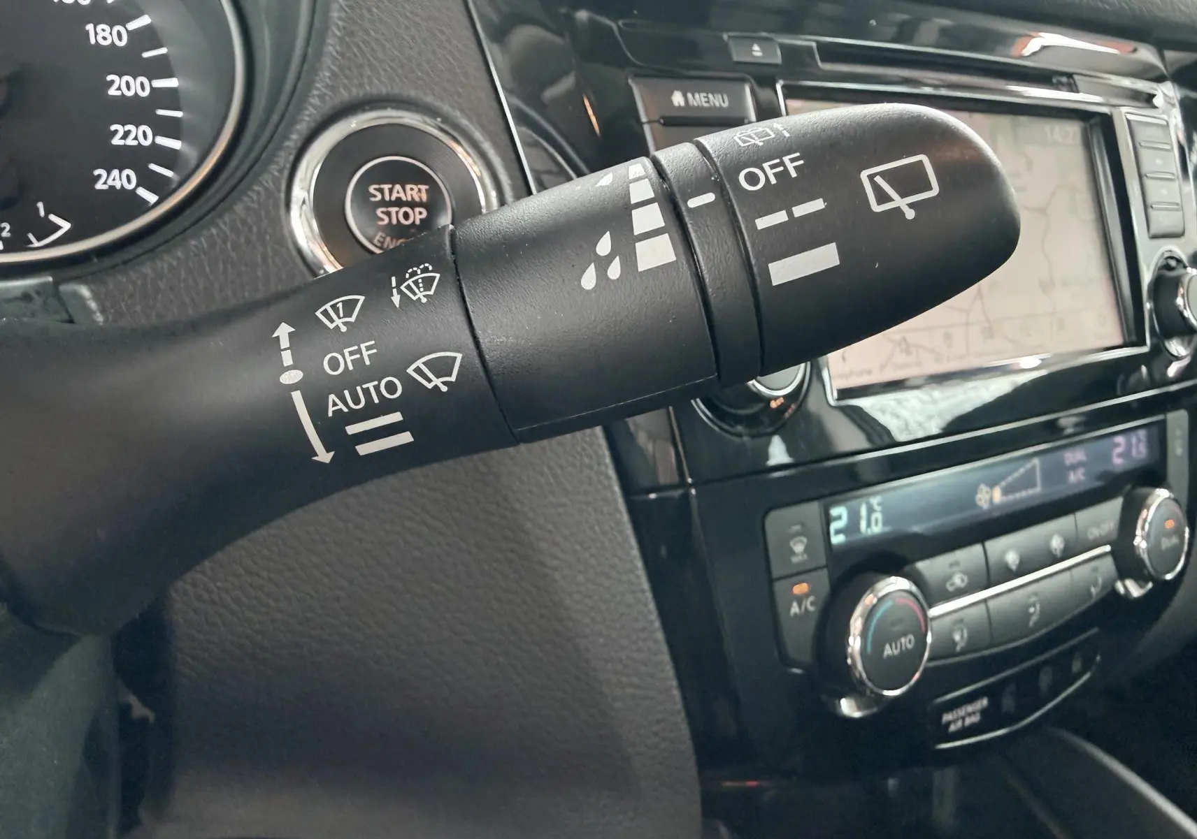 Gros plan sur la commande d’essuie-glace dans l’habitacle noir du Nissan Qashqai, avec tableau de bord et écran tactile en arrière-plan.