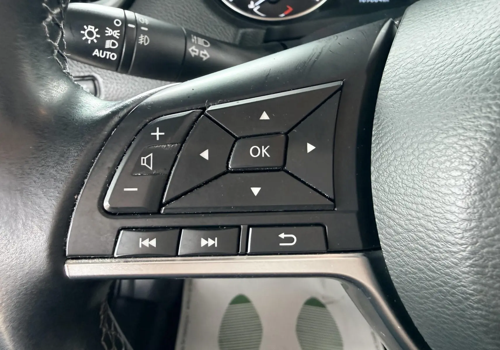 Gros plan sur les commandes gauche du volant noir du Nissan Qashqai 2020, avec boutons de navigation et volume.