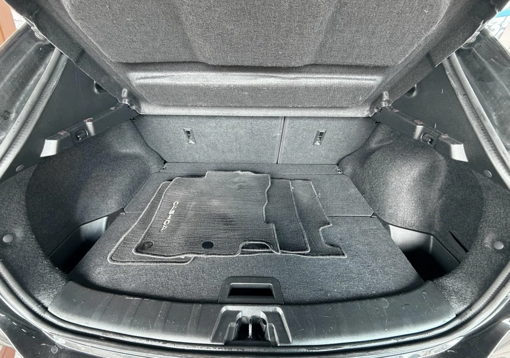 Coffre ouvert vu de l'arrière d'un Nissan Qashqai noir avec tapis de sol noir à l'intérieur.