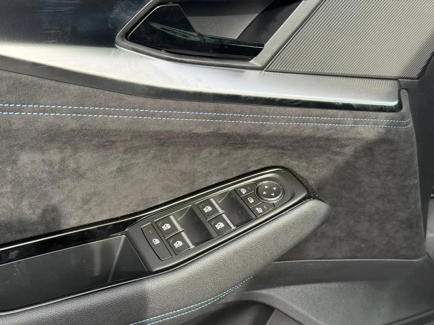 Gros plan sur la porte côté conducteur du Renault Austral 2026, revêtement gris foncé avec surpiqûres bleues et commandes vitres.