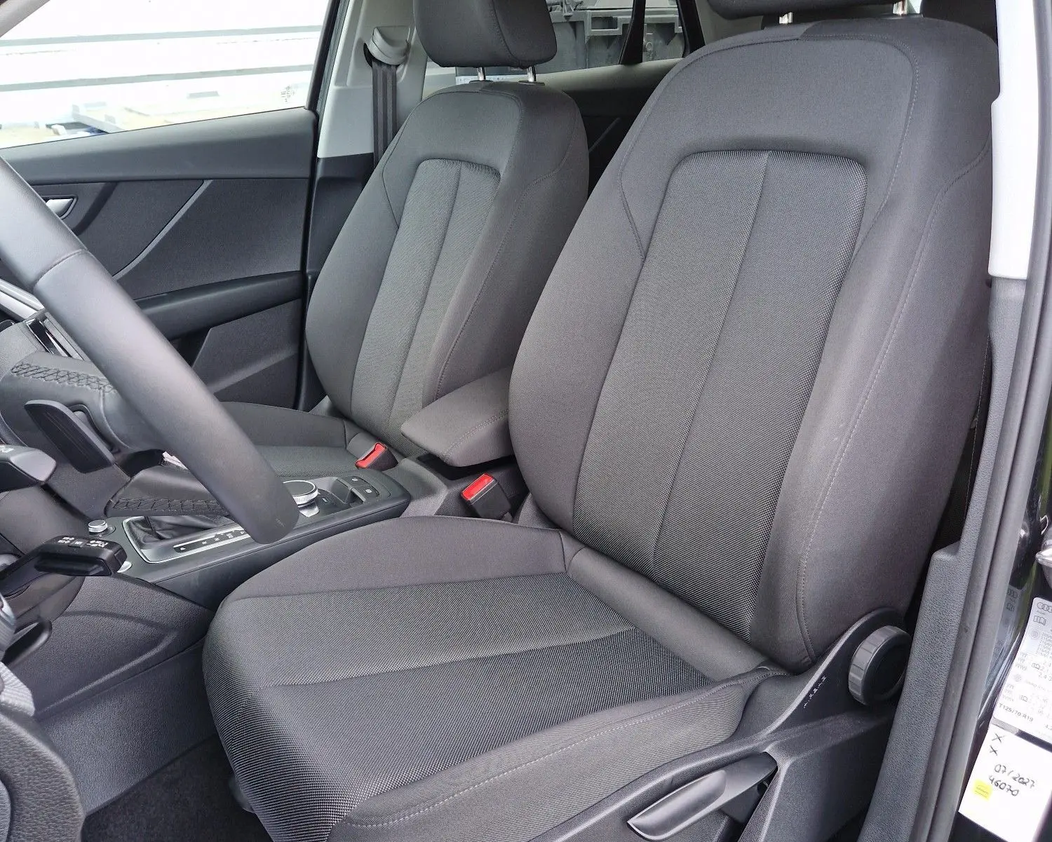 Vue intérieure côté conducteur de l'Audi Q2 35 TFSI 150CH en tissu noir, montrant les sièges avant et la console centrale.