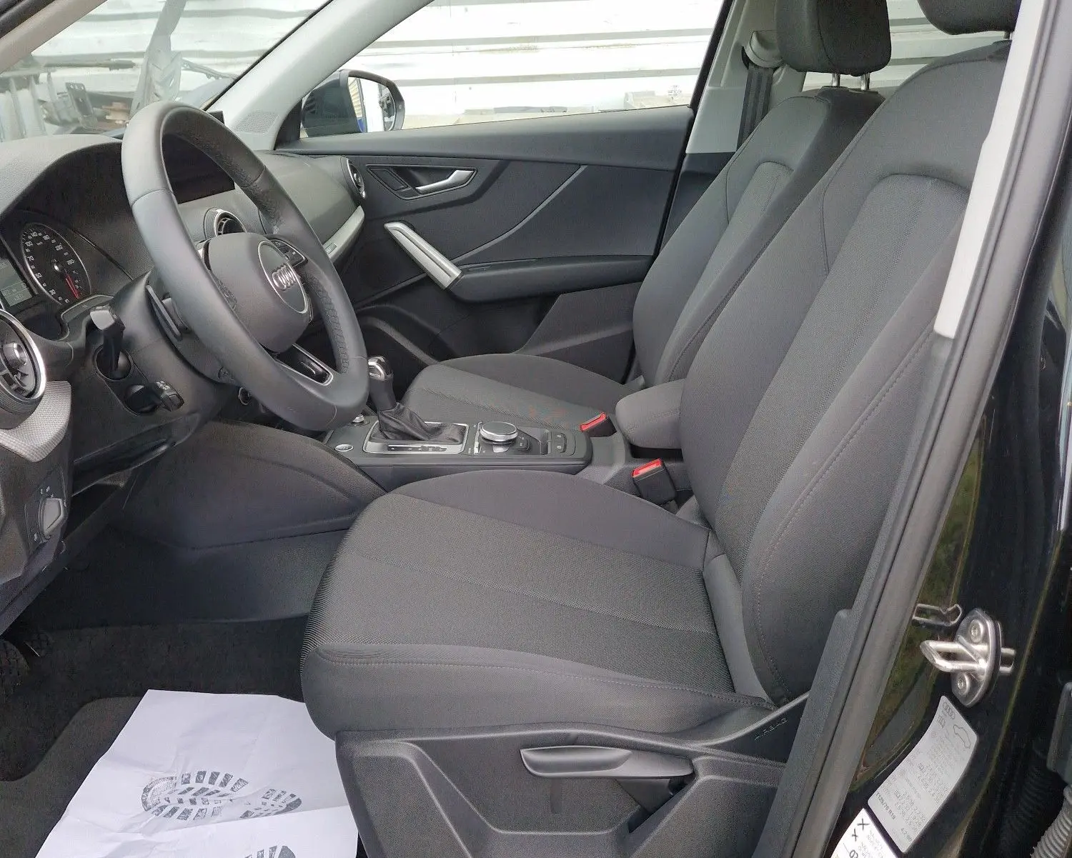 Intérieur côté conducteur d’Audi Q2 noir mito metal 2023, sièges tissu noir et volant multifonction visible.