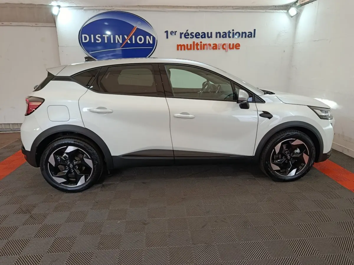 Profil latéral gauche d'un Renault Captur blanc 2025 avec jantes noires et détails noirs contrastants.