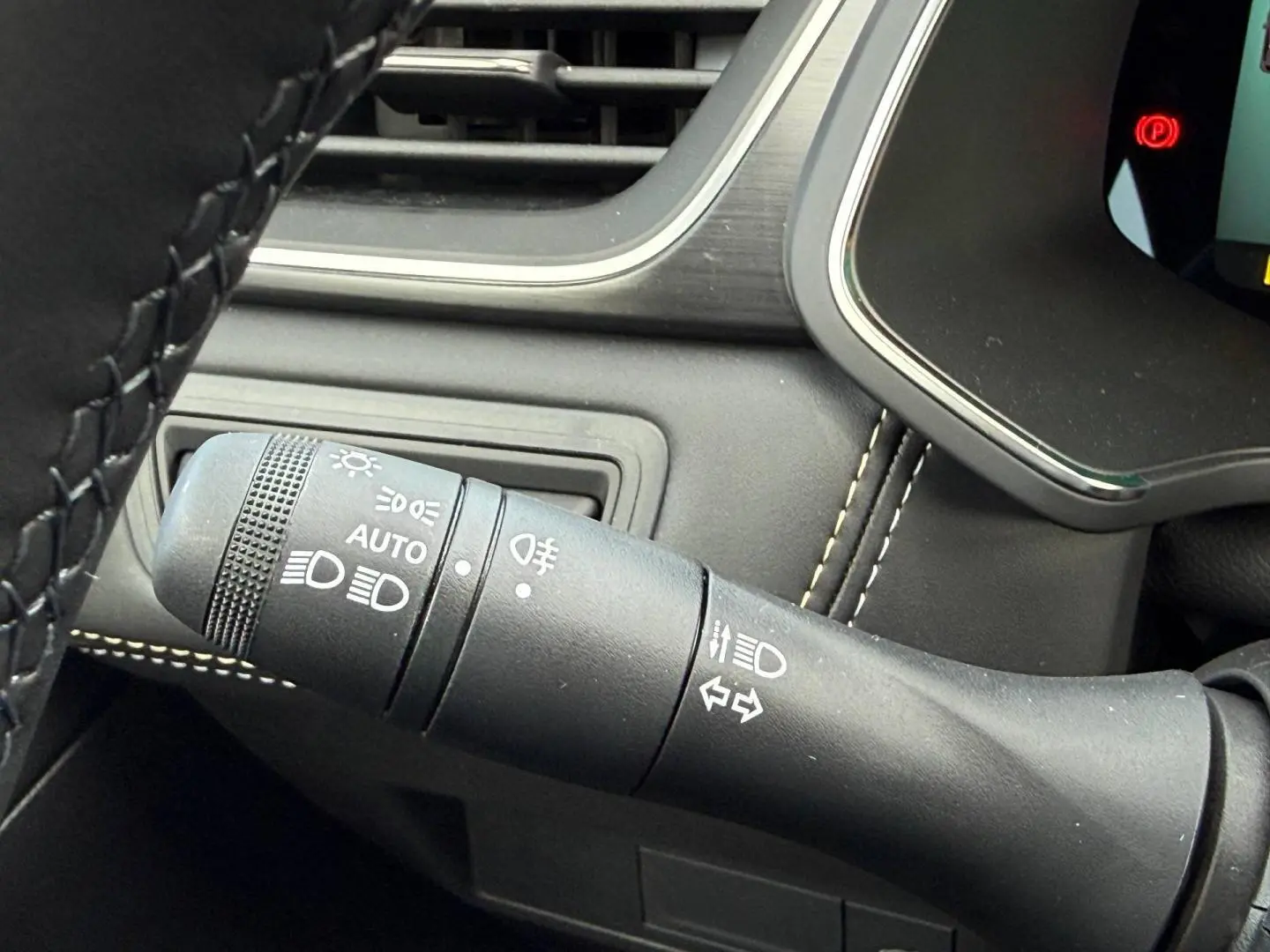 Gros plan sur la commande des phares et clignotants du Renault Symbioz gris Rafale, avec coutures blanches visibles.
