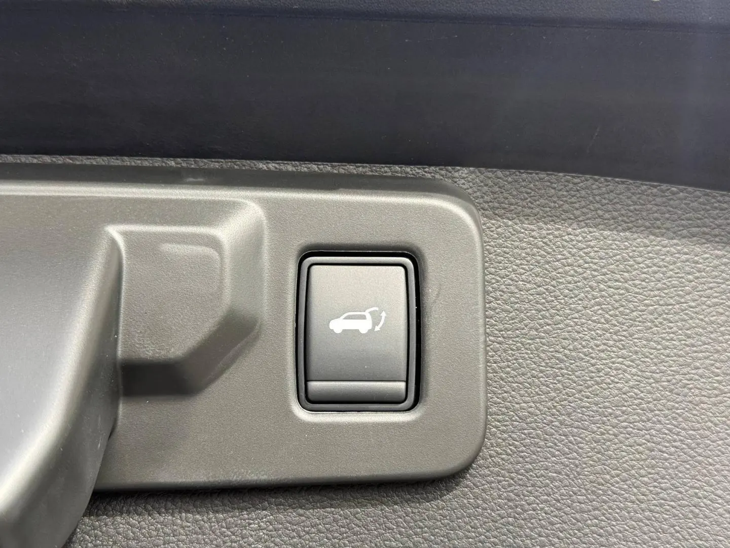 Bouton intérieur de commande d'ouverture électrique du coffre sur Renault SYMBIOZ gris, vue rapprochée du panneau de porte.