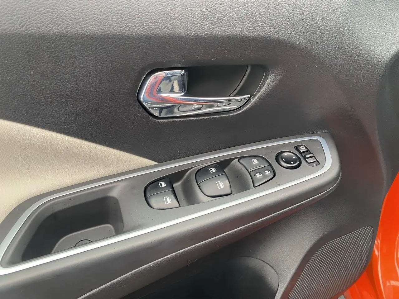 Gros plan sur la porte avant gauche de la Nissan Micra orange Energy, montrant les commandes des vitres et la poignée chromée.