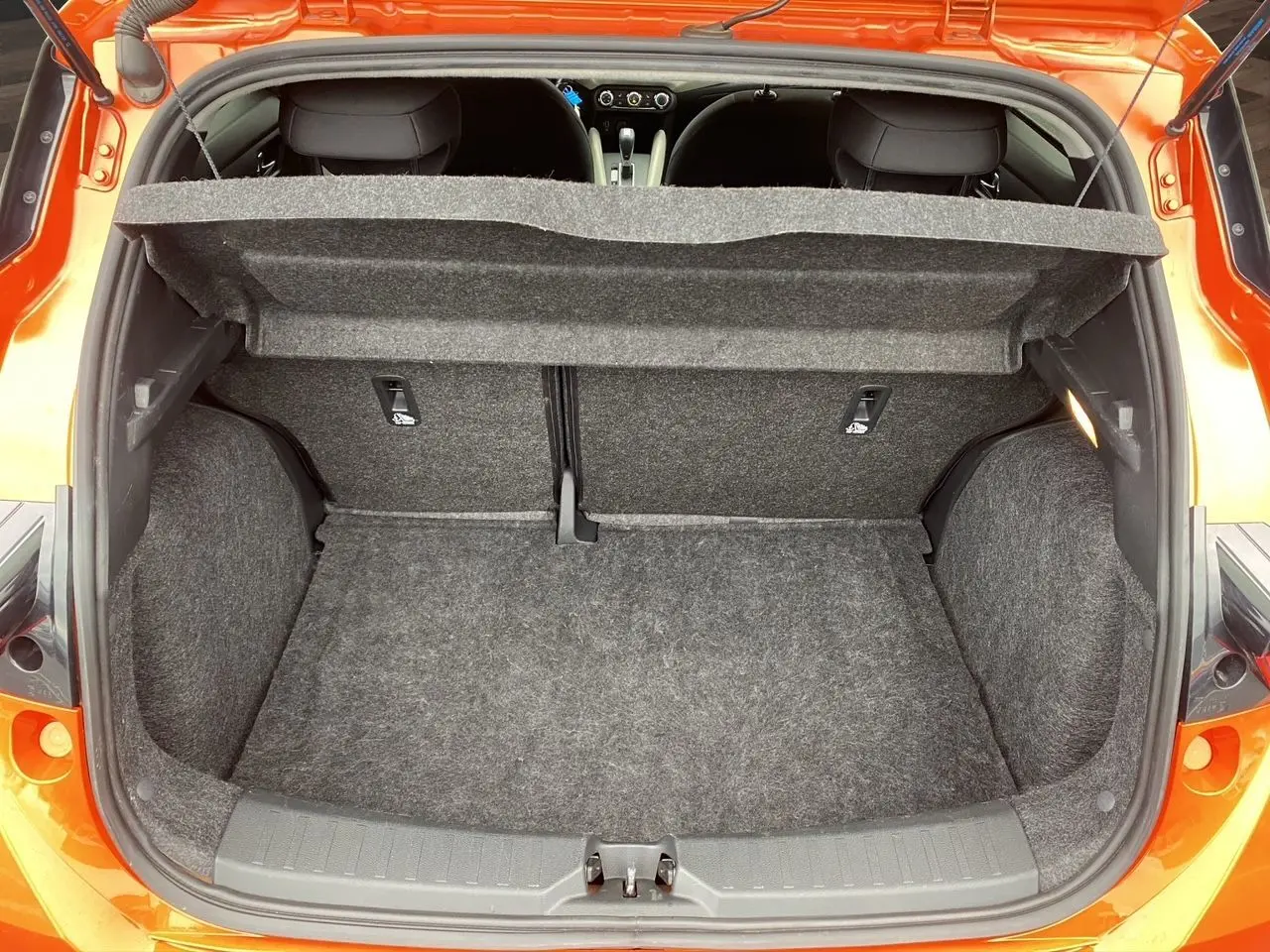 Vue arrière du coffre ouvert d'une Nissan Micra orange Energy 2022, montrant l'espace de chargement vide et la plage arrière relevée.