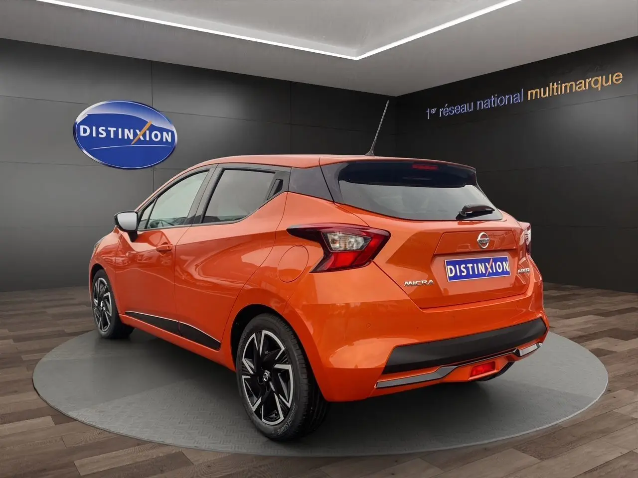 Vue 3/4 arrière droite d'une Nissan Micra 2022 orange Energy avec jantes noires et toit noir en showroom.
