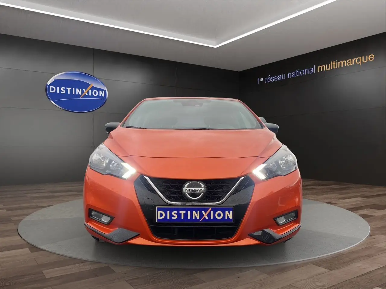 Vue de face d'une Nissan Micra 2022 orange Energy avec phares allumés dans un showroom Distinxion.