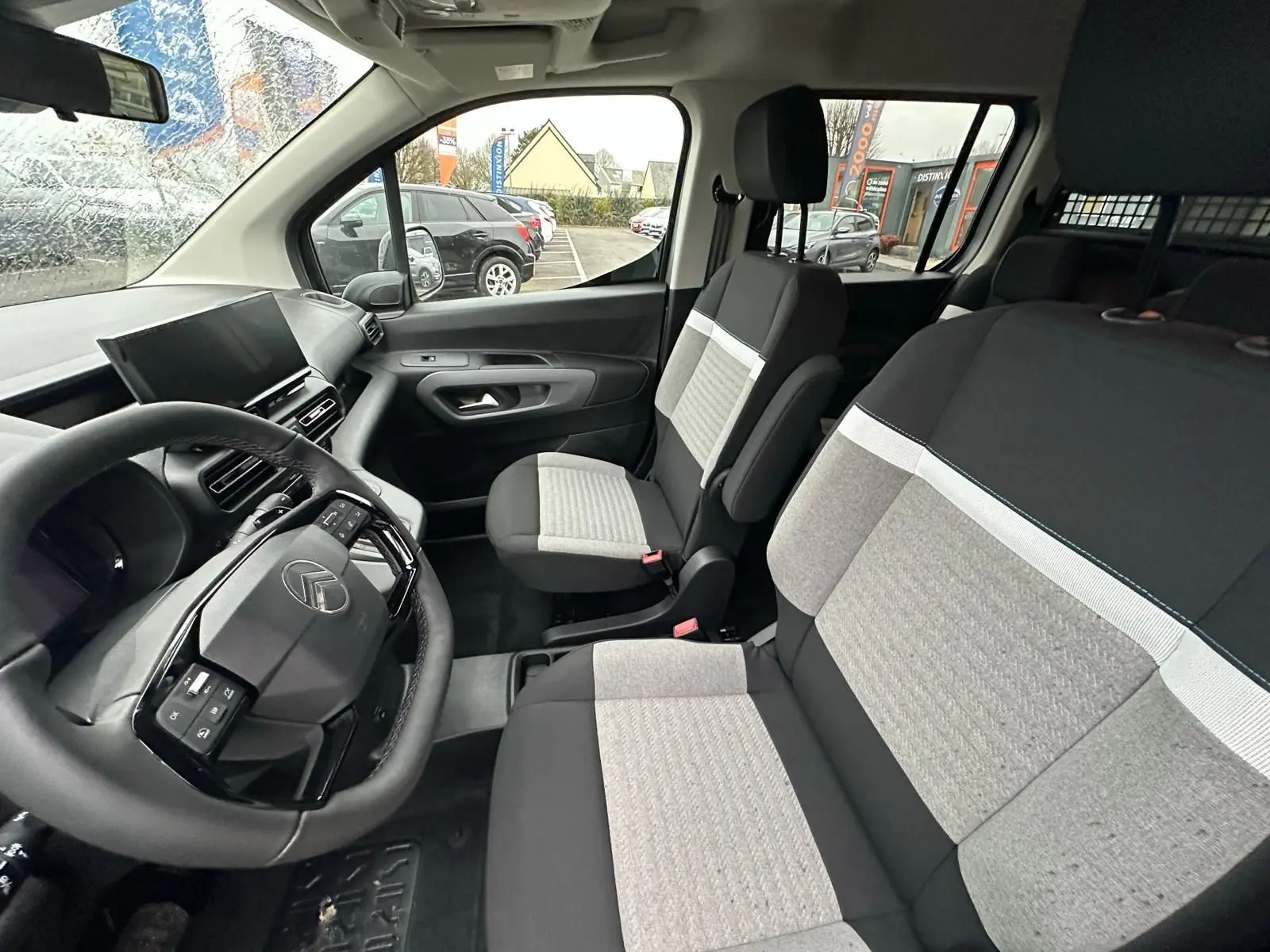 Vue intérieure côté conducteur du Citroën Berlingo 2025, montrant le volant, tableau de bord et sièges bicolores gris et noir.