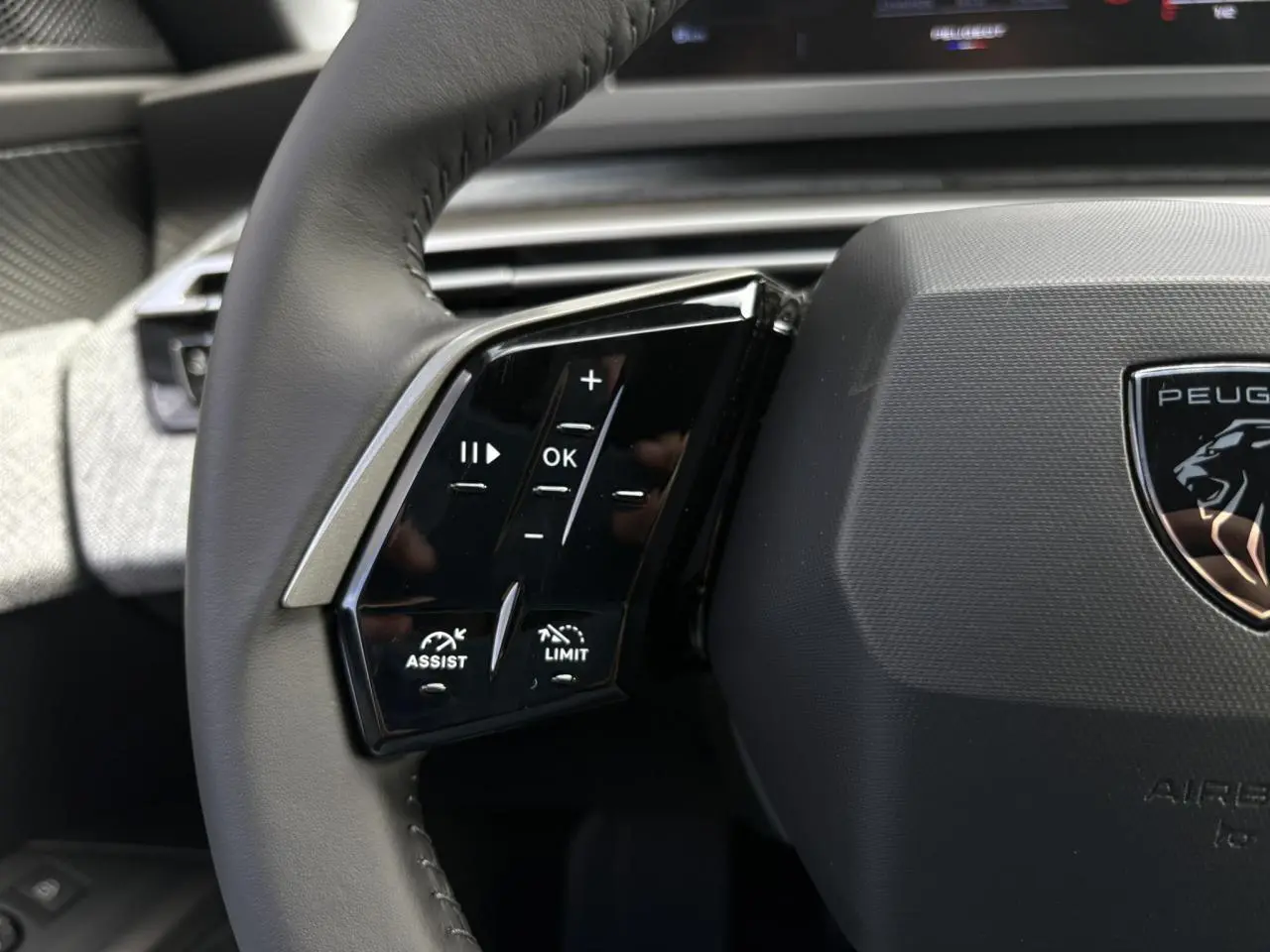 Gros plan sur le volant noir du Peugeot 5008 Hybrid 145 Allure 2025, avec commandes intégrées et logo lion central.
