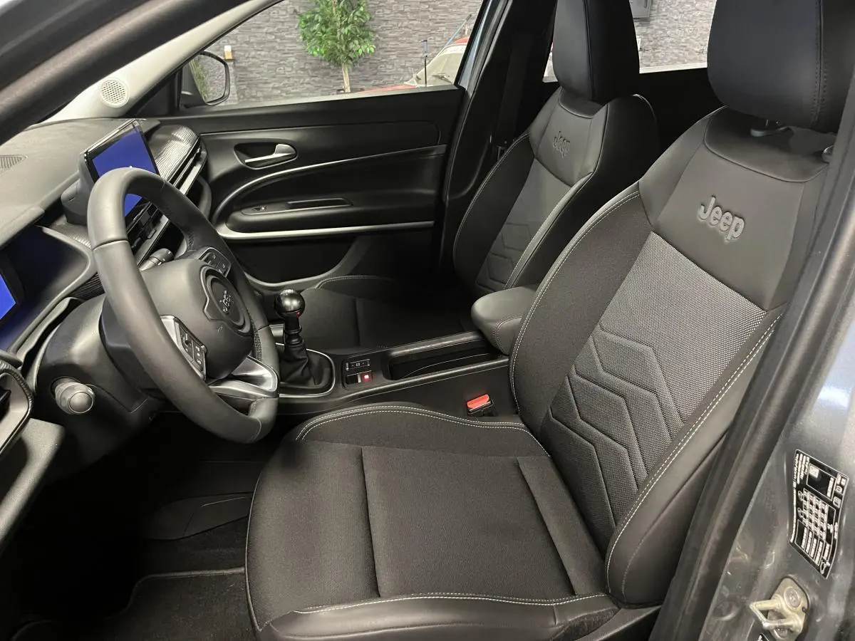 Vue intérieure côté conducteur du Jeep Avenger gris, mettant en valeur les sièges mixte tissu/TEP noir avec logo Jeep brodé.