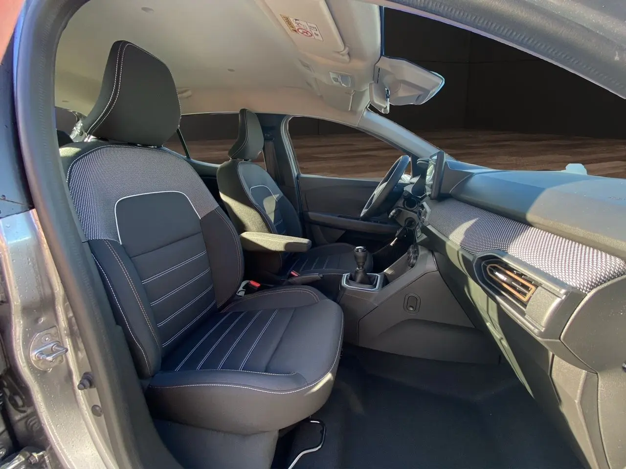 Vue intérieure côté conducteur de la Dacia Sandero Stepway 2025 gris schiste, sièges noirs et tableau de bord moderne.