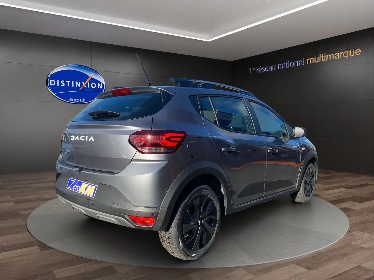 Vue 3/4 arrière droite d'une Dacia Sandero Stepway gris schiste avec barres de toit et feux LED allumés.
