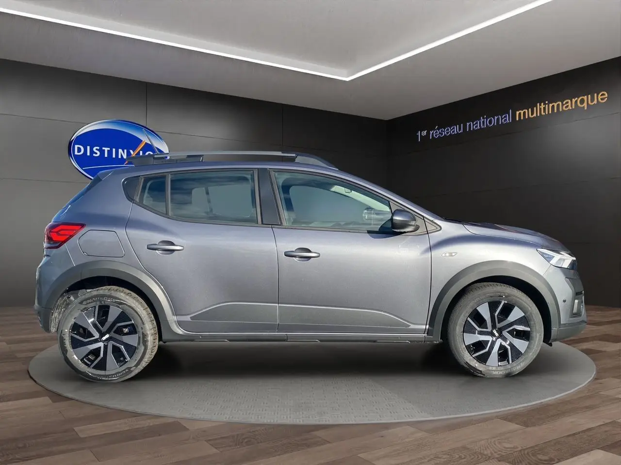 Vue latérale droite d'une Dacia Sandero Stepway gris schiste avec barres de toit et jantes modernes en concession.