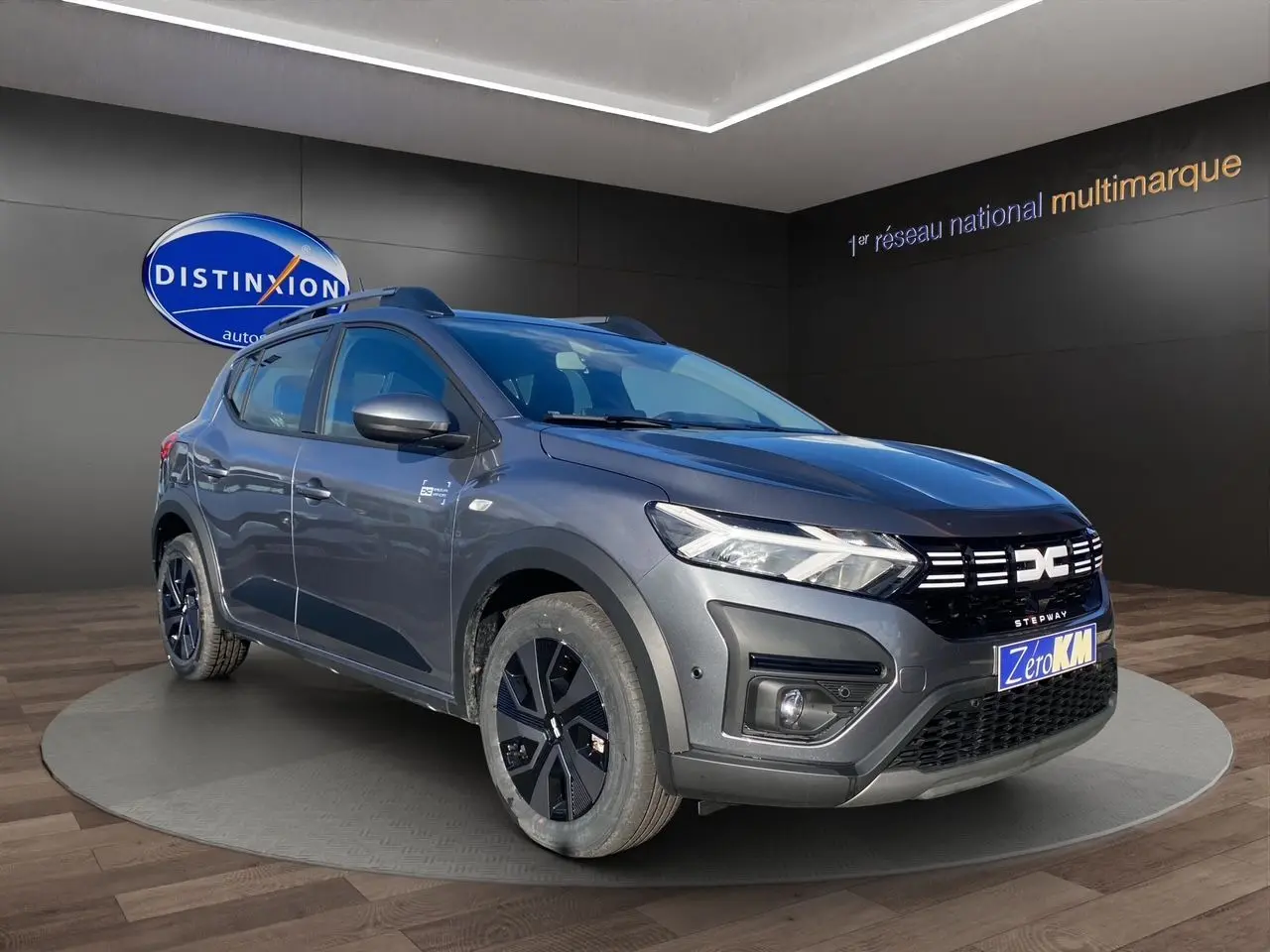 Dacia Sandero Stepway gris schiste en 3/4 avant droit, avec barres de toit et jantes noires distinctives.