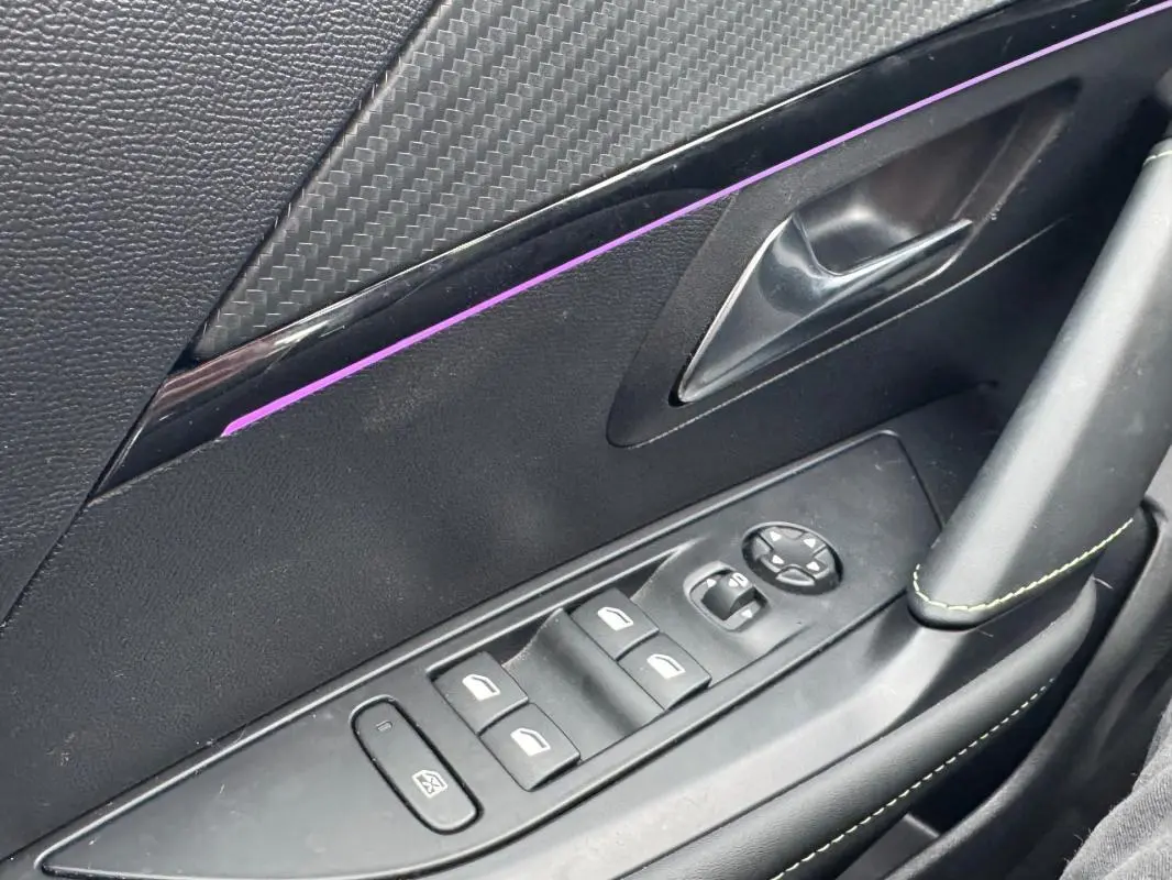 Détail de la porte côté conducteur du Peugeot 208 gris, montrant les commandes des vitres électriques et le bouton de réglage des rétroviseurs.