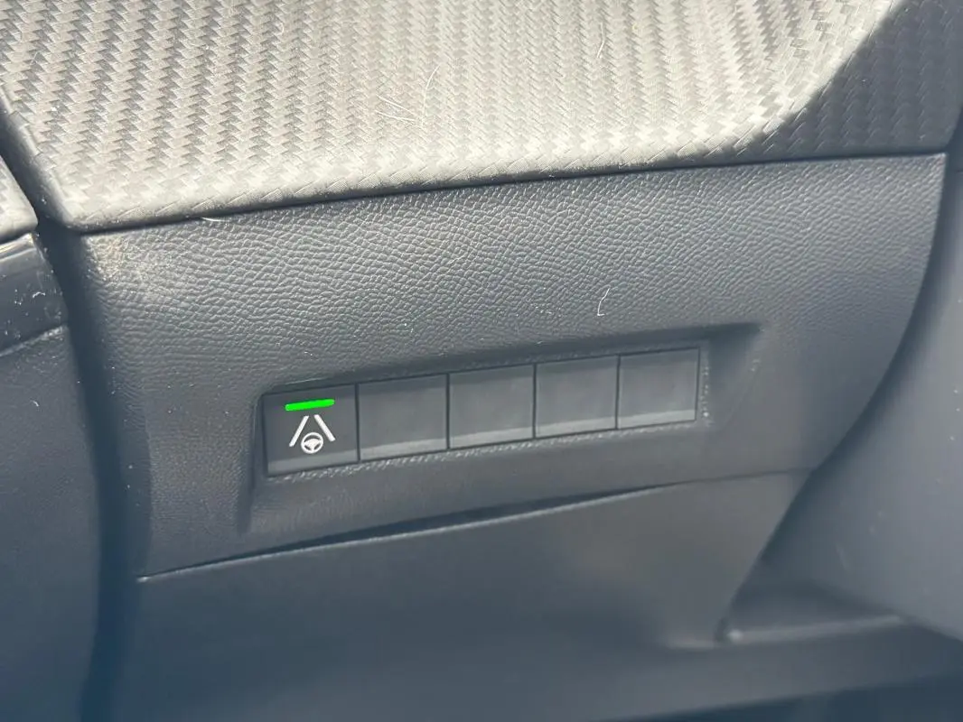 Gros plan sur le tableau de bord noir du Peugeot 208 Hybrid 110, montrant un bouton d’aide au maintien de voie activé.