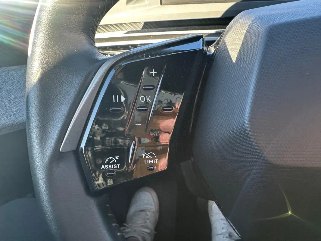 Gros plan sur les commandes à gauche du volant du Peugeot 3008 Hybrid blanc, avec boutons de réglage et assistance.