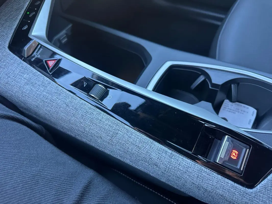 Gros plan sur la console centrale du Peugeot 3008 Hybrid blanc, avec frein à main électrique et habillage tissu gris.