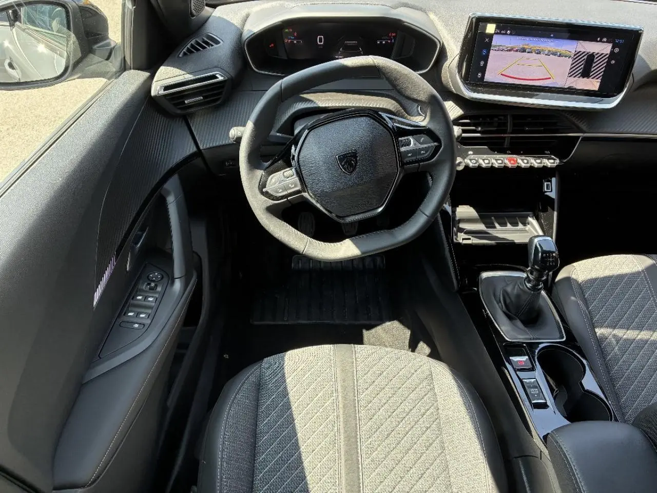 Vue intérieure de face du poste de conduite du Peugeot 2008 1,2 100 CV Allure 2024, volant compact et écran tactile avec caméra de recul.