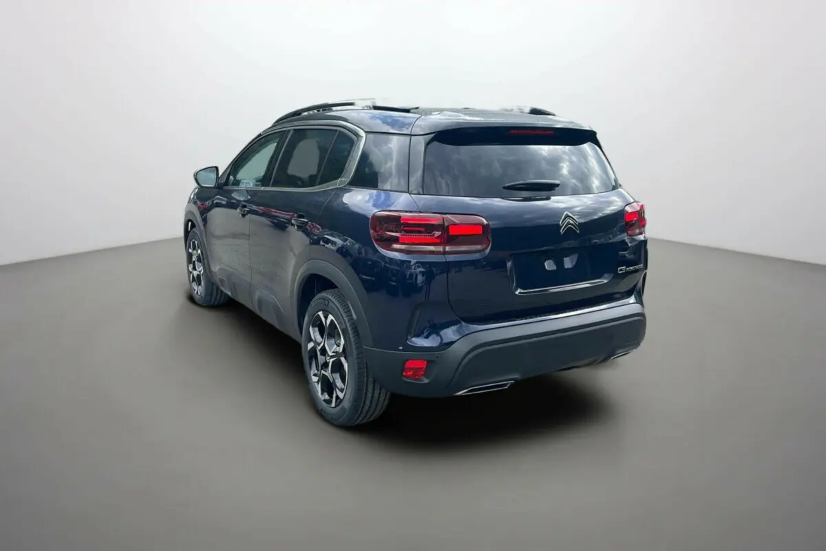 Vue 3/4 arrière gauche d'un Citroën C5 Aircross 2025 hybride bleu Eclipse avec toit noir et jantes stylisées.