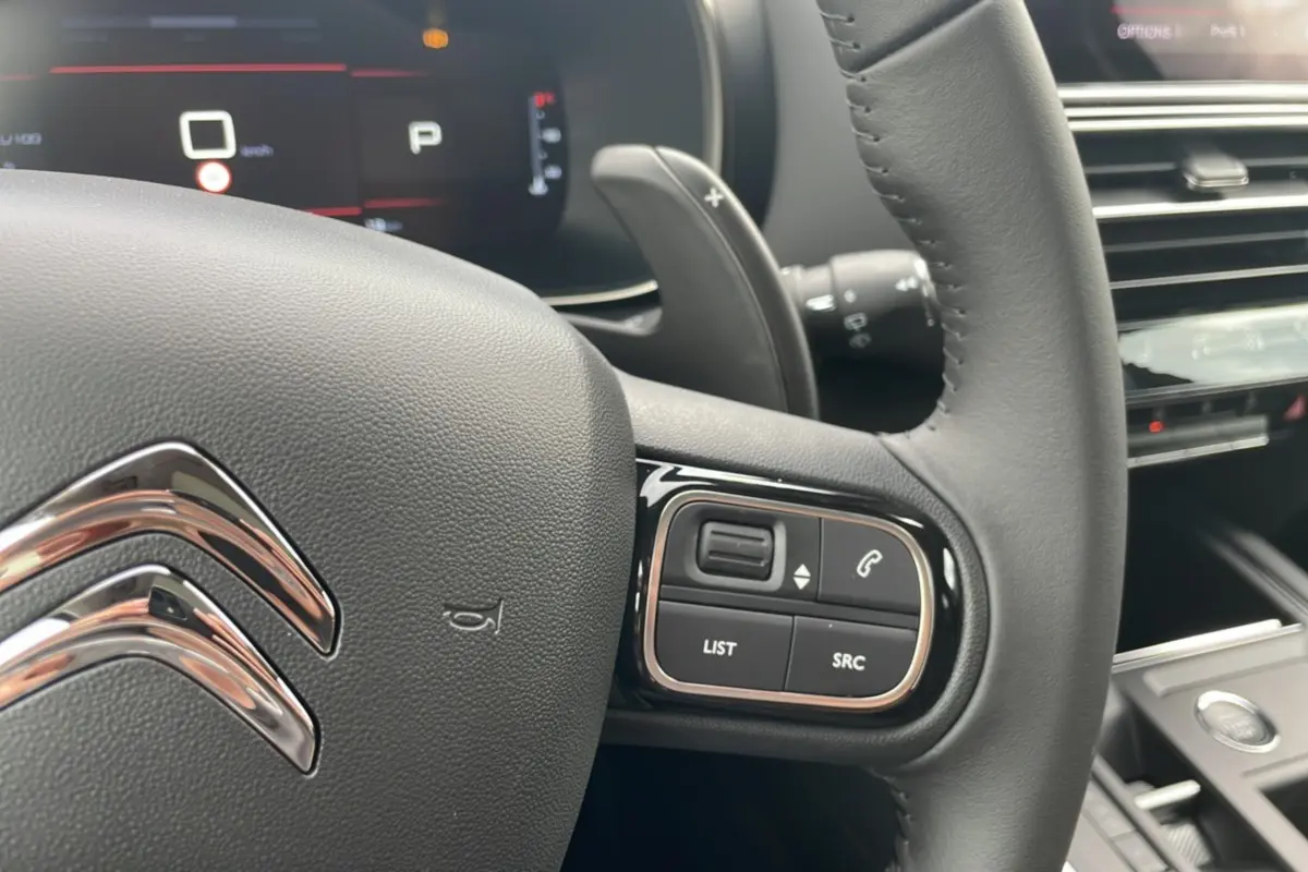 Gros plan sur le volant en cuir du Citroën C5 Aircross Hybrid 2025, avec commandes intégrées et tableau de bord numérique.