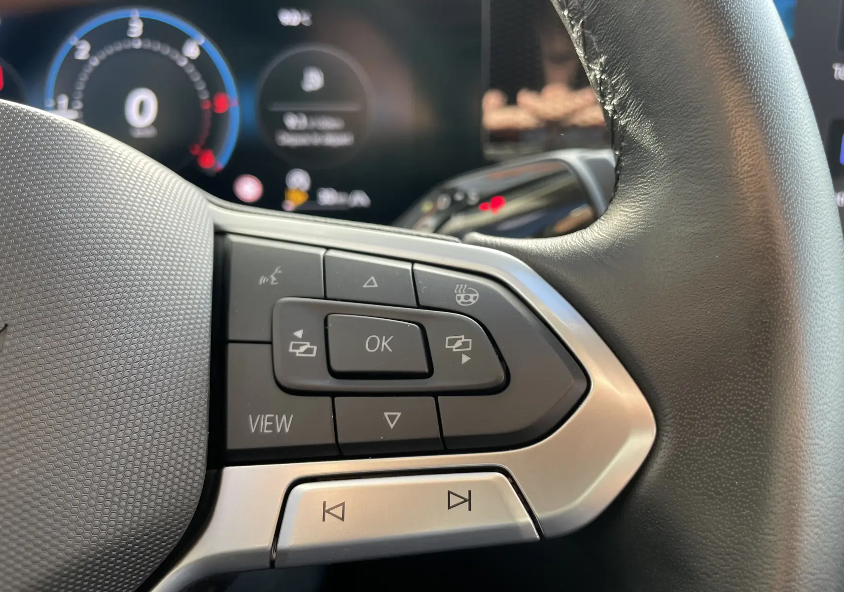 Gros plan sur les commandes gauche du volant cuir noir du Volkswagen Tiguan 2024, boutons multifonctions visibles.