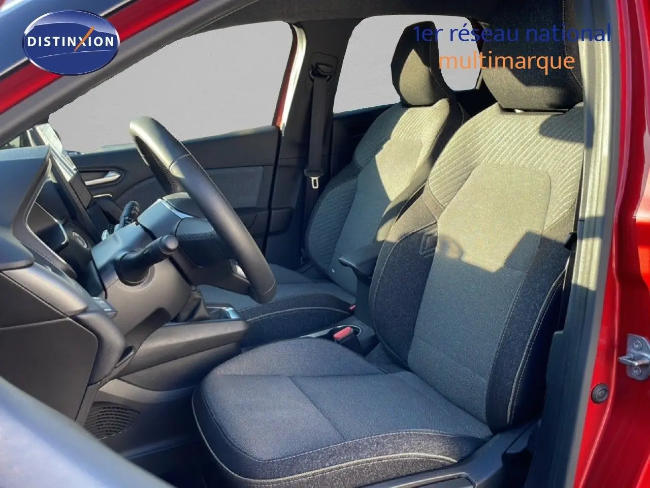 Vue intérieure côté conducteur du Renault Captur rouge désir métal, sièges tissu gris et volant noir visible.