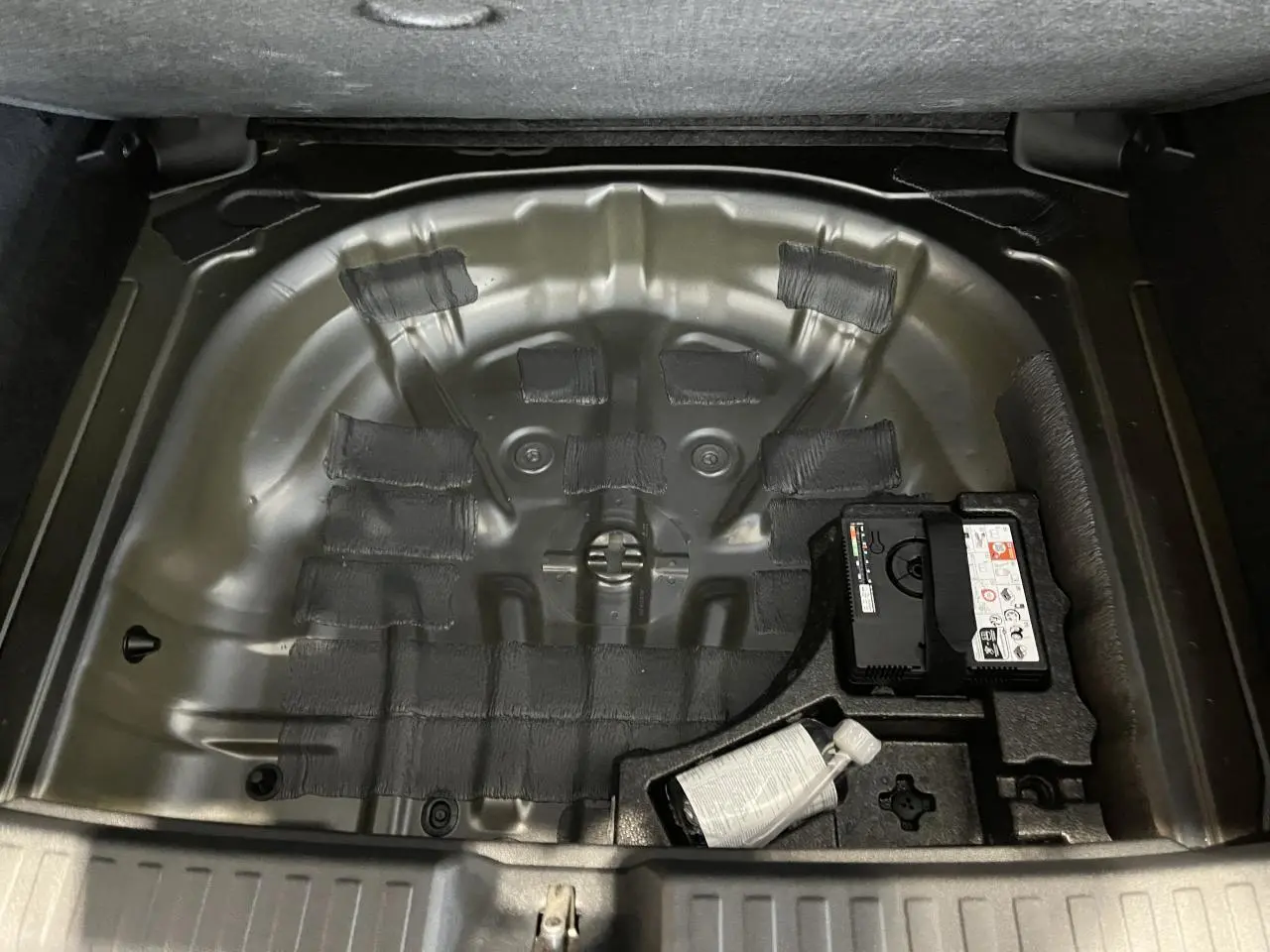 Coffre ouvert en vue plongeante montrant le rangement sous plancher vide avec kit de réparation sur Audi A3 Sportback gris.