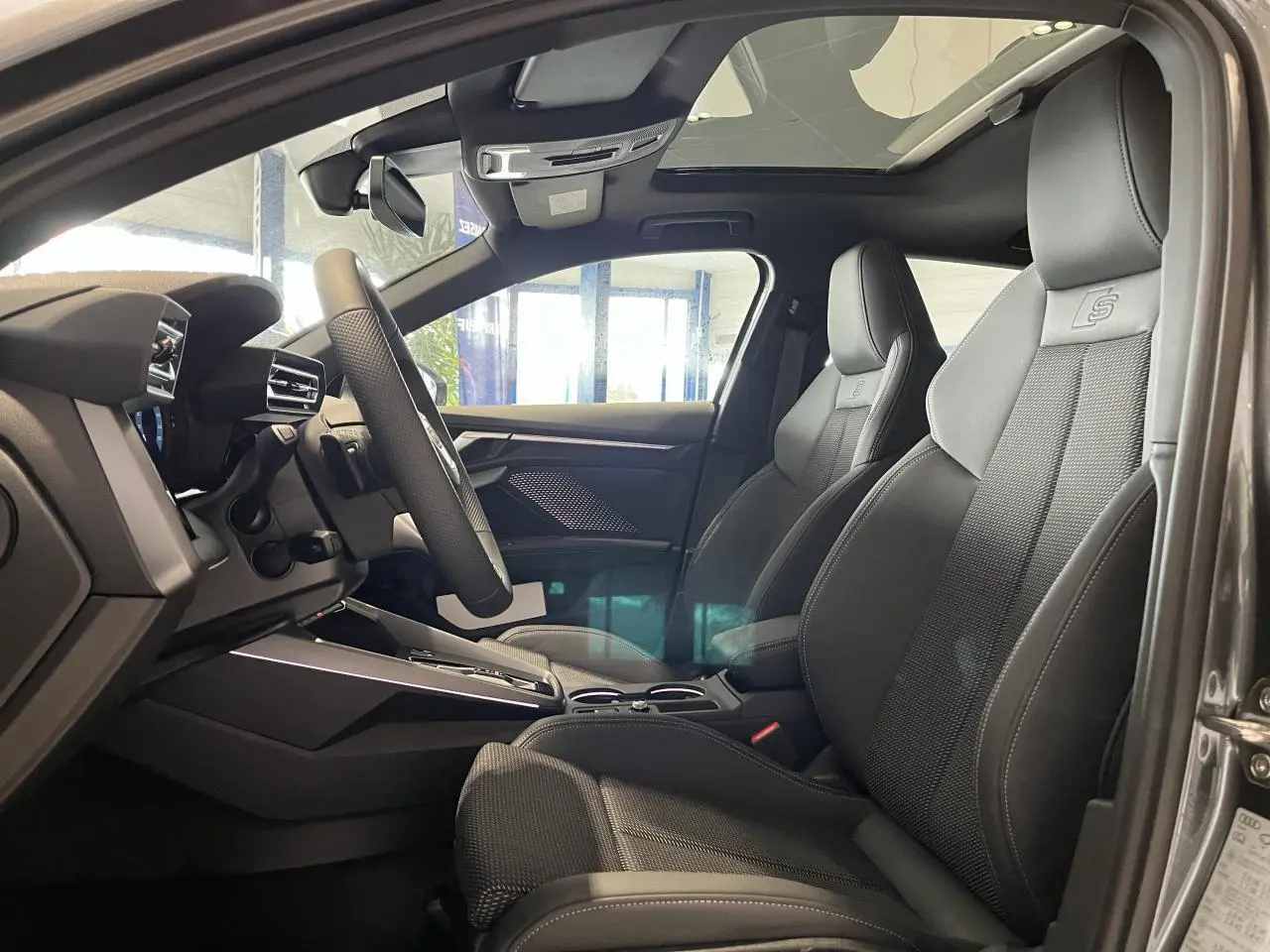 Vue intérieure côté conducteur de l’Audi A3 Sportback gris, sièges sport S line en cuir avec logo embossé et toit ouvrant panoramique.