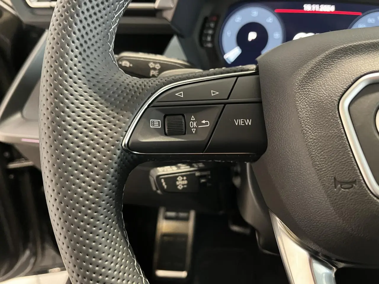 Gros plan sur le volant cuir perforé multifonctions de l'Audi A3 Sportback 2025 avec commandes intégrées et tableau de bord numérique.