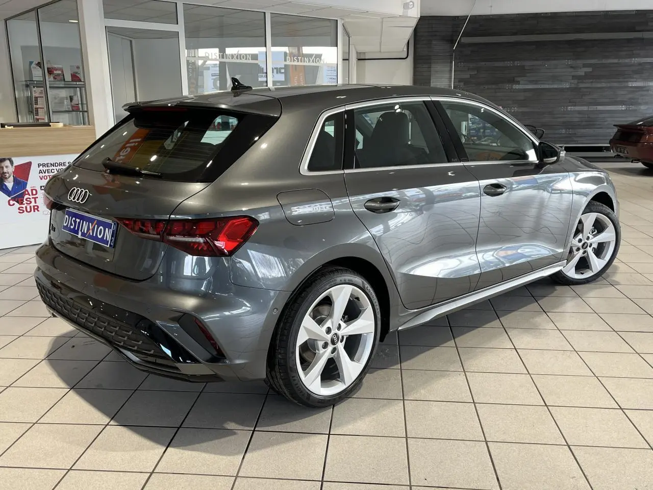 Audi A3 Sportback gris métallisé vue 3/4 arrière droit en intérieur avec jantes 5 branches et toit ouvrant panoramique.